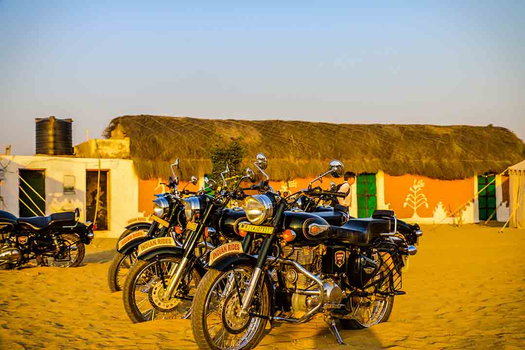 A view of Royal Enfields against the rustic Rajasthan I Village view of Rajasthan & motorbikes I India on Royal Enfield Tour