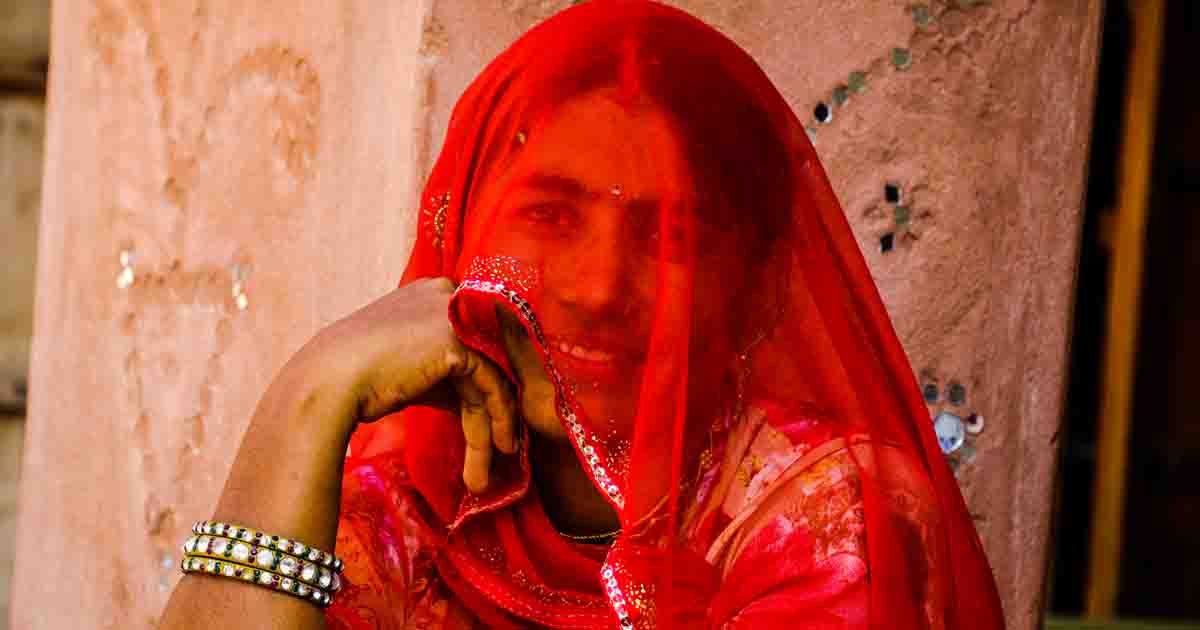 An Indian woman from rural India in a veil, wearing bright red colored attire, and jewelry I Rajasthani Village life on Bike